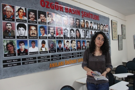 Günay Aksoy har arbetat som journalist och redaktör på Özgür Gündem i fyra år. Här står hon framför en poster på redaktionen med namn och bilder på tidningens medarbetare som har dödats.