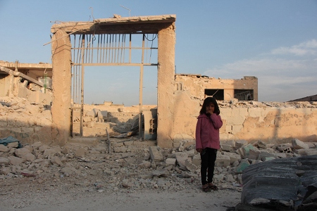 En sjuårig skolelev står framför hennes förstörda skola i Idlib i oktober 2016.