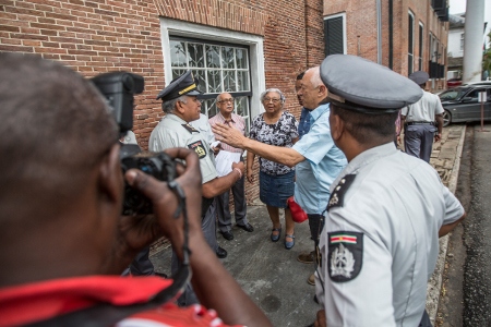 Utanför Högsta domstolens byggnad vid Onafhankelijksplein i Paramaribo samlas anhöriga till offren för decembermorden inför en domstolsförhandling. Hetsig ordväxling mellan anhöriga och polis om vem som ska släppas in i rättssalen uppstår.