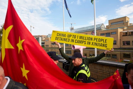 En Amnestyaktivist i Haag skyddas av polis mot prokinesiska demonstranter som i oktober 2018 samlats för hälsa Li Keqiang, Kinas premiärminister välkommen, under hans besök i Nederländerna.