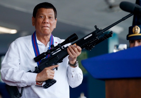 President Rodrigo Duterte håller upp ett gevär vid ett besök på Camp Crame 19 april 2018. Dutertes uppmaningar till krig mot narkotikan har skördat många människoliv sedan 2016.