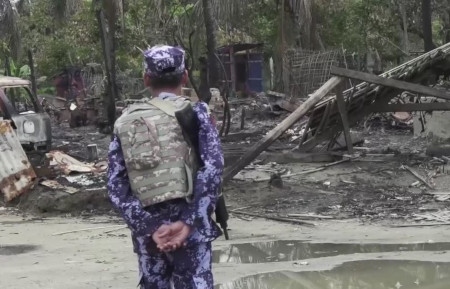 En medlem i Myanmars gränsvaktsstyrka framför ett nedbränt hus 21 september 2017.