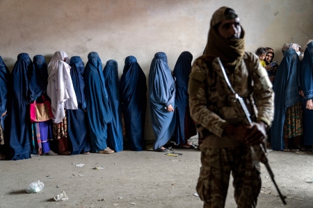 En talibansoldat håller vakt medan kvinnor köar i Kabul för att få livsmedelshjälp från en humanitär hjälpgrupp.